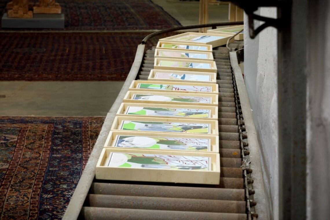 Opere su carta incorniciate disposte lungo una rampa nella sala espositiva