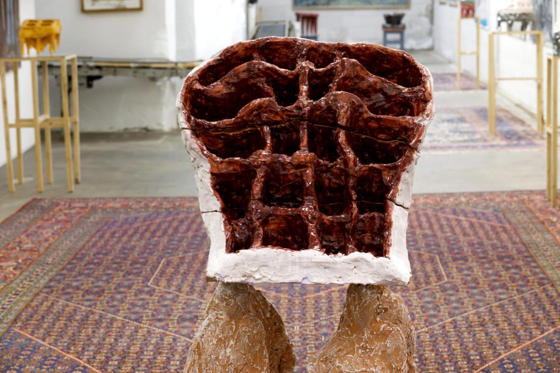 Scultura bordeaux della serie In Bilico vista frontalmente, con il corridoio espositivo sullo sfondo
