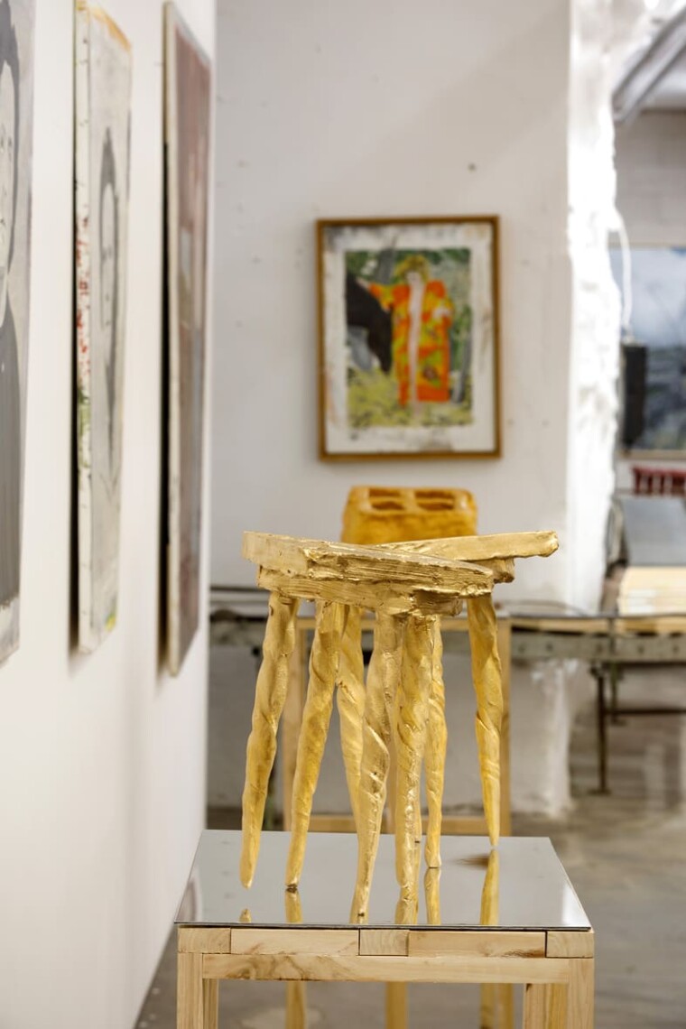 Scultura dorata a forma di sgabello su basamento, accanto a un dipinto incorniciato