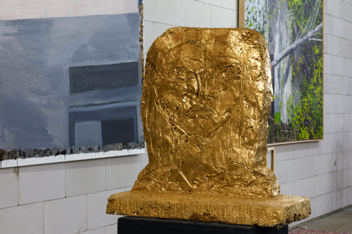 Scultura dorata a forma di testa su basamento nero