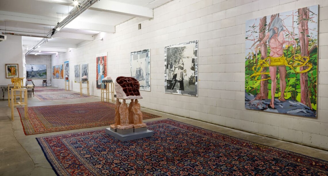 Veduta della sala espositiva con dipinti e scultura bordeaux su tappeti persiani