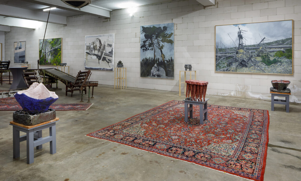 Veduta della sala espositiva con scultura blu e sgabello bordeaux della serie In Bilico su tappeti persiani