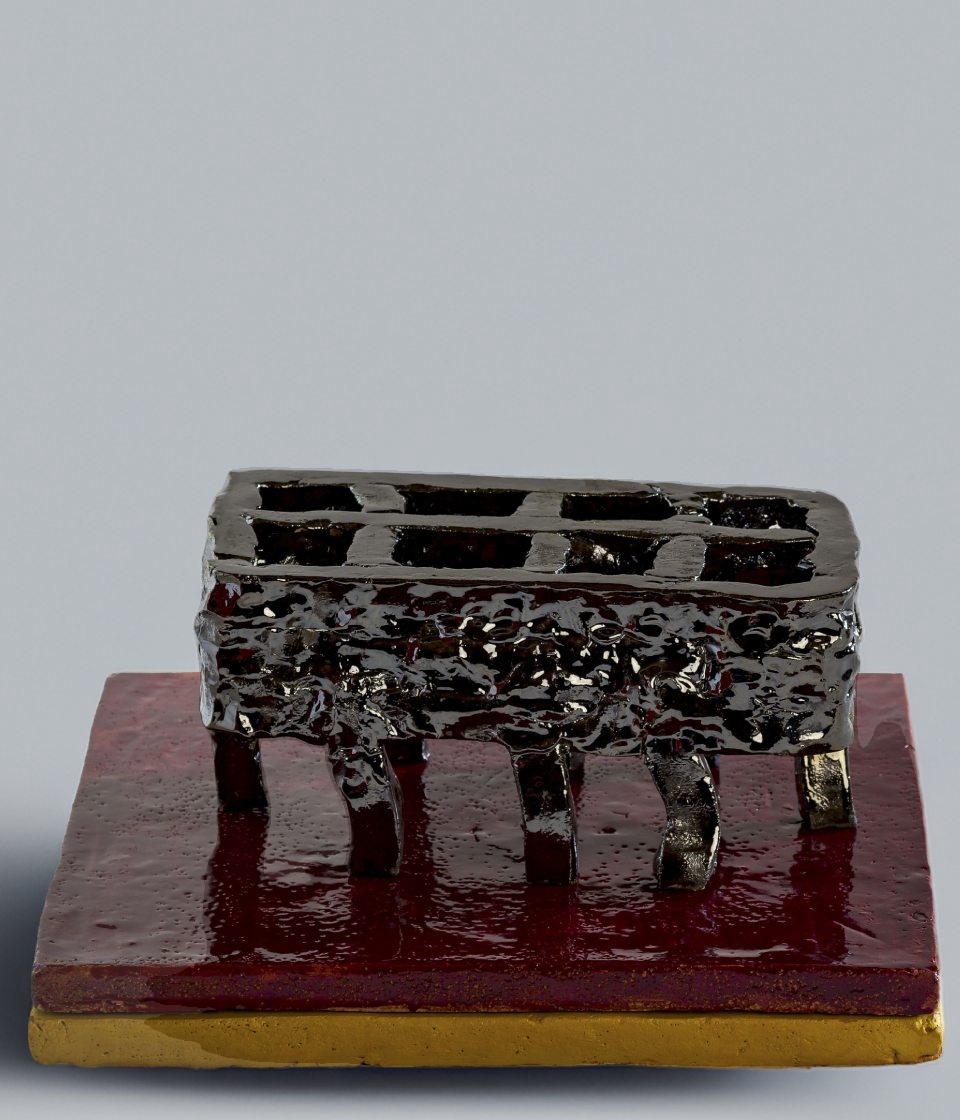 Scultura rettangolare in ceramica nera specchiata con una griglia aperta sulla parte superiore, simile a un braciere o a una struttura industriale arcaica. La superficie è densa e grumosa. Poggia su gambe ricurve sopra una base quadrata bordeaux lucida con bordo inferiore dorato.